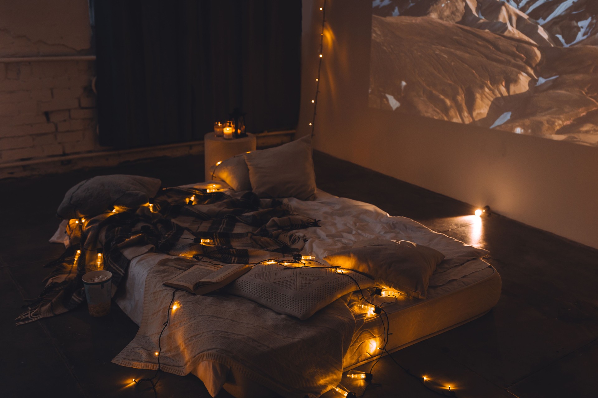 Romantic surprise for girlfriend or boyfriend on Saint Valentine's Day. Bedroom prepared for watching old movies, decorated with lights and burning candles. Cozy home Christmas atmosphere
